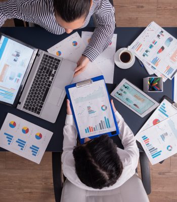 Top viewTop view of manager and employee doing teamwork in business office , looking at charts on laptop display. Finance paperwork with charts at workplace. Discusing financial plan.